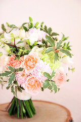 Wedding round bouquet with white freesia flower, green dianthus, peach roses, light chrysanthemum and fresh greens. Bridal bouquet and wood on pink background. Front view, closeup, vertical photo.