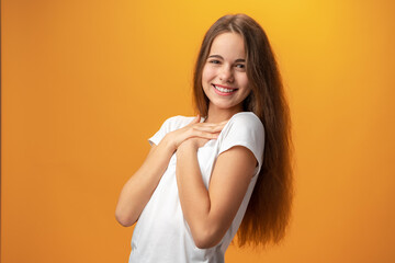 Beautiful grateful teen girl with hands on chest against yellow background