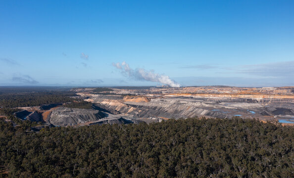 open cut coal mine with coal-fired power station on horizon and native forest in foreground