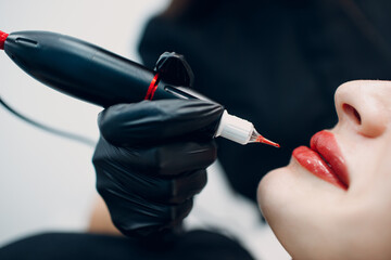 Cosmetologist applying red permanent make up tattoo on female lips. - obrazy, fototapety, plakaty