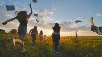 Cheerful students run throwing notebooks after school at sunset. - obrazy, fototapety, plakaty