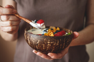 Woman eating healthy breakfast from coconut bowl. Eco friendly and zero waste tableware. Yogurt...