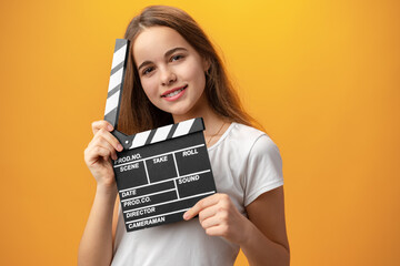 Smiling teen girl holding clapper board against yellow background