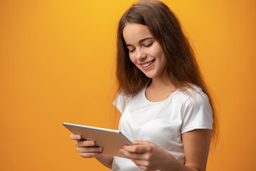 Fototapeta premium Beautiful teen girl using digital tablet over yellow studio background