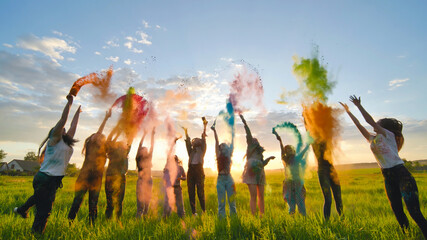 Cheerful girls toss up multi-colored powder at a beautiful sunset. - obrazy, fototapety, plakaty