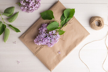 Craft envelope with a purple lilac branch on a light wooden table. Top view, flat lay. Rustic style.  Romantic concept for presents.