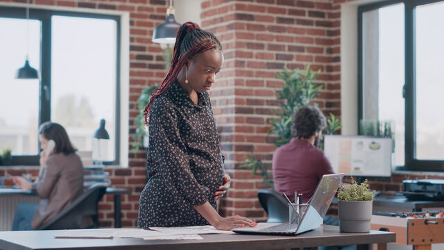African american woman expecting child and working on business project with documents. Pregnant employee analyzing files to design and plan marketing strategy for development at office.