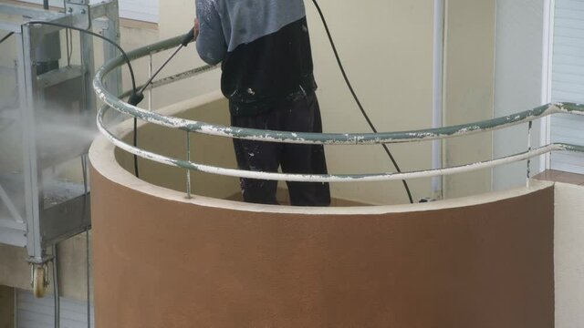 A man uses a high-pressure machine to disinfect the walls of a multi-storey building for subsequent repairs. On an industrial paint hoist.