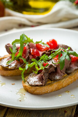 Bruschetta with roast beef, tomatoes and aragula on white plate, vertical, macro close up
