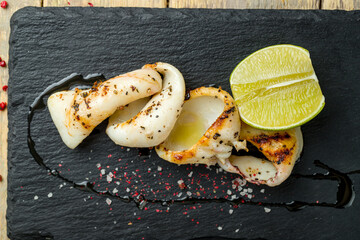Roasted squid on black stone with lime top view