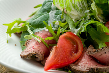 Salad with roast beef, vegetables and greens on white plate on wooden table, macro close up
