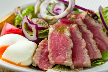 Nicoise with tuna, poached egg and vegetables on wooden table macro close up