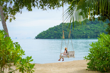 girl relaxing on a swing on the beach in summer alone on vacation