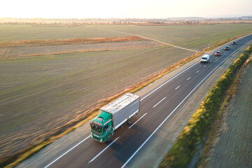 Aerial view of semi-truck with cargo trailer driving on highway hauling goods in evening. Delivery transportation and logistics concept