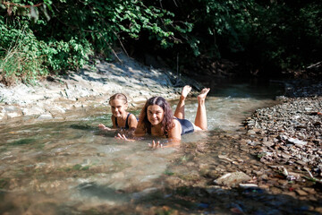 Happy girl with her mother bathing in stream canyon river in the mountains, nature pool. Cold water, hardening and natural spa procedure, wildlife and green tourism, summer holidays