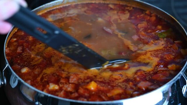 Stirring boiling soup in a saucepan close-up. Traditional Russian delicious meat soup Solyanka. Cooking soup at home. Slow motion 4k.