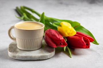 Bouquet of tulip flowers and cup of coffee on gray background.
