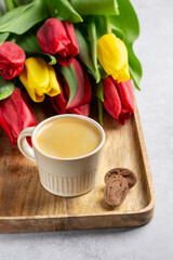 Fototapeta na wymiar Bouquet of tulip flowers and cup of coffee on wooden tray on gray background.