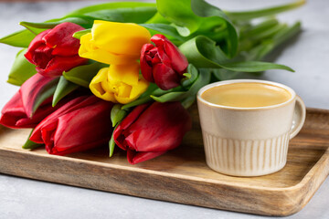 Bouquet of tulip flowers and cup of coffee on wooden tray on gray background.