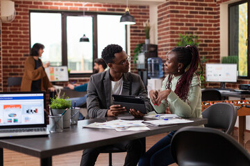 Corporate entrepreneurs analyzing marketing statistics using tablet computer working at company project during business meeting in startup office. Diverse team brainstorming ideas planning strategy
