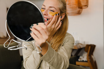 Blonde white woman applying eye patches while looking in mirror