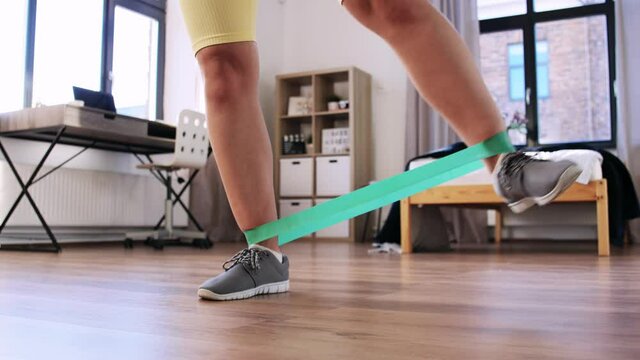 sport, fitness and healthy lifestyle concept - legs of young woman or teenage girl exercising with resistance band at home