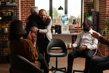 Psychologist giving hug to man after sharing recovery progress with people at aa meeting. Woman therapist and person hugging and celebrating addiction achievement at therapy session.