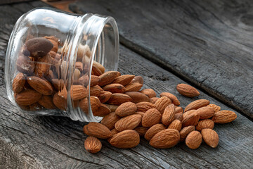 A rustic scene featuring a glass jar overflowing with roasted almonds and Brazil nuts, spilling...