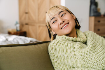 Asian teen girl with piercing smiling while resting on sofa