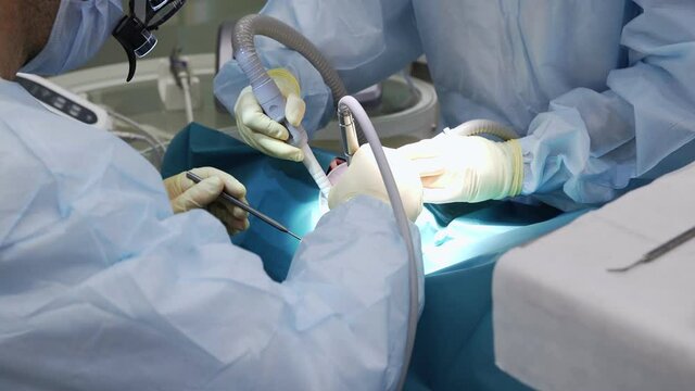 Professional doctors performing dental surgery, treating teeth in the patient's mouth. Surgical operation. Dentistry.