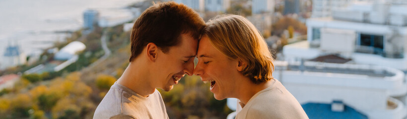 Fototapeta premium European gay couple laughing while standing head to head on balcony
