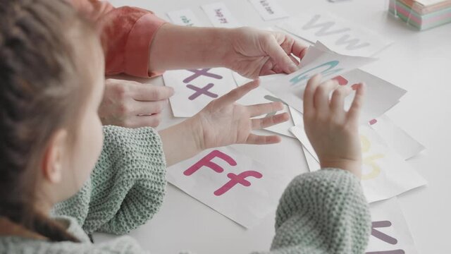 Top view slowmo shot of little girl using cards with colorful letters while learning alphabet together with female teacher