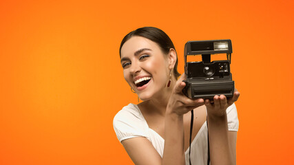 Positive woman holding vintage camera isolated on orange.