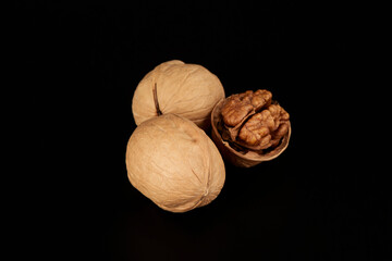 Two walnuts in shell and odi without shell lies next to each other in a black background