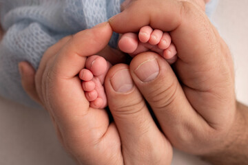 The palms of the father, the mother are holding the foot of the newborn baby in a blue blanket. Feet of the newborn on the palms of the parents. Photography of a child's toes, heels and feet.