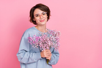 Portrait of attractive cheerful cute girl holding flowers copy blank space isolated over pink pastel color background