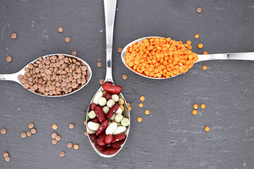 Hintergrund gesundes Essen - ein Löffel voll Erbsen, Linsen und Bohnen auf grauem...