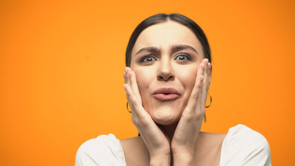 Amazed woman in blouse touching face isolated on orange.