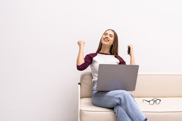 Portrait of happy woman sitting on floor and looking at laptop screen, holding phone and card,...