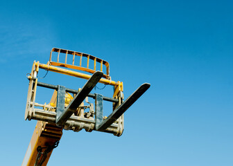 Telehandler with raised boom and forks on clear blue sky background © Iryna
