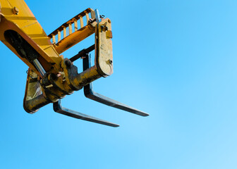 Telehandler with raised boom and forks on clear blue sky background