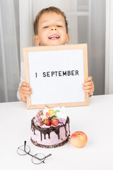 adorable happy cheerful boy in glasses show letter board with text 1 September, festive cake with ABC. Knowledge day. Concept of education, back to school. Selective focus