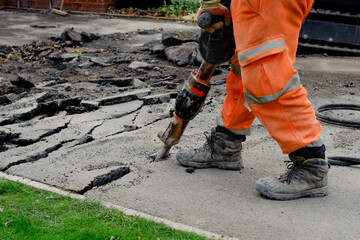Construction worker breaking road gully using hydraulic breacker during road works on new housing...