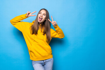 Young woman standing isolated over blue background showing peace gesture.