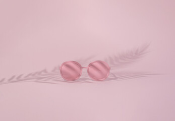 Sun glasses and palm leaf silhouette against bright pink background. Minimal summer beach concept.  Holidays, exotic vacation idea. Good relaxing. 