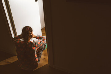 A little girl huddled in a corner and cries, covering her eyes and ears with her hands, because her...