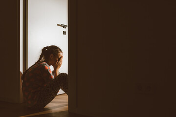 A little girl huddled in a corner and cries, covering her eyes and ears with her hands, because her...