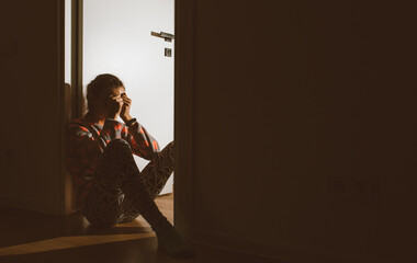 A little girl huddled in a corner and cries, covering her eyes and ears with her hands, because her...