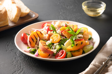 Panzanella salad with tomatoes, bread, cheese and peach in white bowl on black background. Italian cuisine. Vegetarian panzanella salad. Mediterranean healthy food. Close up.