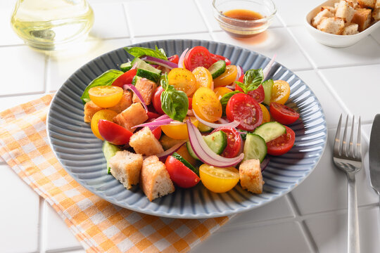 Piquant Panzanella with tomatoes, cheese and croutons in plate on white kitchen table. Italian cuisine. Vegetarian panzanella salad. Summer vegetables colorful salad.